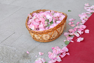cesta de mimbre llena de pétalos  de rosa junto a una alfombra roja y pétalos esparcidos