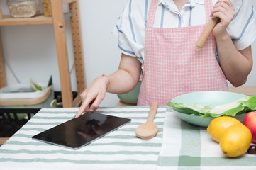 Asian young woman use finger slide on tablet screen prepare ingredients for cooking follow cooking online video clip on website in kitchen,Social distancing, stay at home and work from home concept.