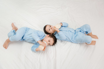 Two baby twin boys in pajamas lie on the bed drinking milk from bottles. View from above. concept of marriage and friendship. concept of baby food.space for text