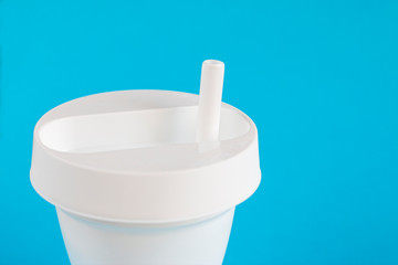 White plastic glass with a lid and a straw on a blue background close-up. Disposable tableware for drinks.