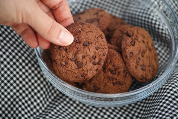 A person taking a baked homemade chocolate chip cookie from a glass bowl.