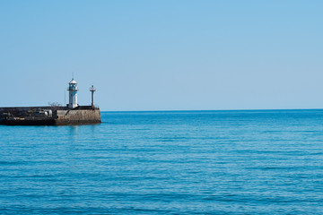 Lighthouse on the background of the sea and the sky, the sea is full calm and clear clear sky, spring. Lighthouse, sea and pier.