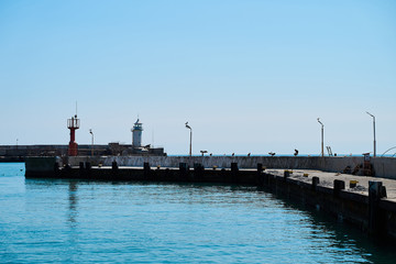 Lighthouse on the background of the sea and the sky, the sea is full calm and clear clear sky, spring. Lighthouse, sea and pier.