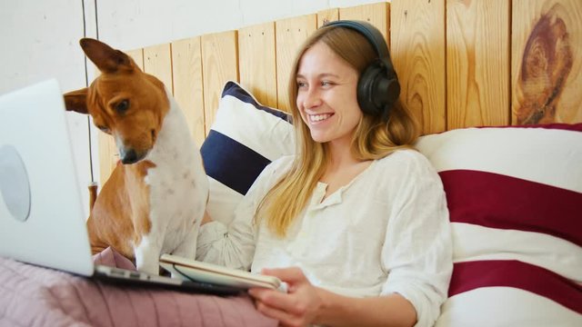 Happy young female pet owner look at laptop with basenji dog. Cute adorable puppy look at comedy funny movie. Girl and her dog have fun, talk to family and friends on video chat conference app