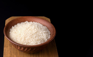 Fototapeta na wymiar Rice in a clay traditional bowl on a wooden board on a black background. Copy space