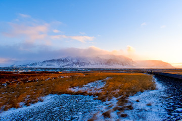 A view from the roadside in Iceland with autumn-colored fields and mountains over the horizon during golden hour