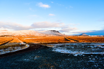 Fototapeta na wymiar The view from a deserted pit stop in Iceland with autumn-colored fields and snow-covered mountains in the horizon during golden hour