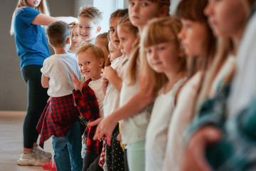 Preparing for a dance class. Group of cute and positive children with young female teacher standing at the dance studio