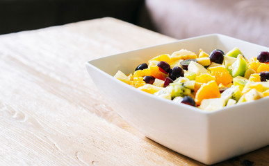 A fruit salad in a white bowl on a wooden table