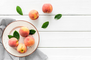 Summer lunch. Red peaches on white wooden background with tablecloth and leaves top-down copy space