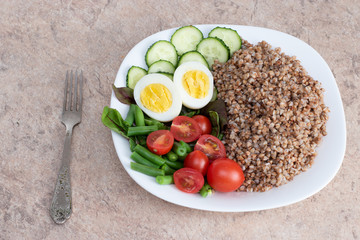 Tasty and healthy food from natural products. Salad of green vegetables, tomato and buckwheat in a white plate. Buckwheat with vegetables and eggs on a white plate.