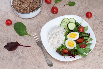 Salad of green vegetables, tomato and rice in a white plate. Rice with vegetables and eggs on a white plate.