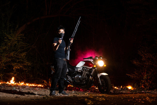 Full Body Of Asian Man Wearing Mask And All Black Uniform Holding Shotgun And Point To Warning Means Stay Home Do Not Get Out With Red Super Bike On Fire In Background