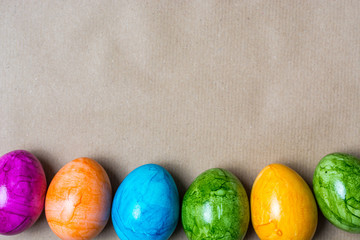 Border of easter eggs in different colors on the bottom on brown paper background
