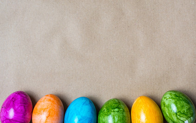 Border of easter eggs in different colors on the bottom on brown paper background