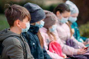 Obraz premium School-age children in medical masks sit on a bench.