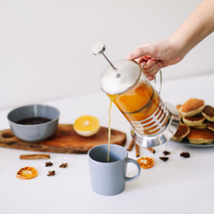 Lush pancakes and teapot with spices, cup of tea with orange, cinnamon, anise. Tasty breakfast on white background. Good morning