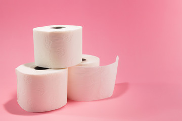 Three rolls of white toilet paper, isolated against pink background, with copy space available next to them.