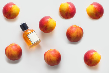 A bottle of peach oil, decorated with a pattern of peaches on a white background. The concept of an aroma oil, the ingredients of an aroma oil, or aromatherapy.
