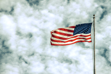 United States of America red white and blue flag blowly crisply in a breeze on top of a flag pole against dramatic cloudy sky - copy space