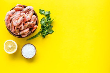 Shrimps for mediterranean salad - with lemon and greeenery - on yellow desk top view copy space