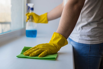 Men's hands in yellow gloves wash the window with a rag and detergent with a spray. Home cleaning. Disinfection.