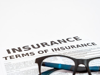 Close up shot of an eyeglass with insurance papers on white background.
