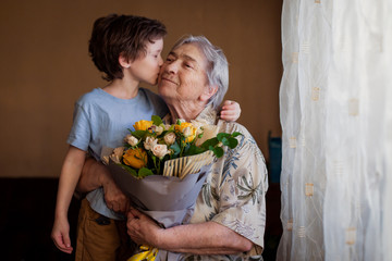 Cute boy wishes an elderly woman a happy birthday. Grandson gives grandmother flowers for the...