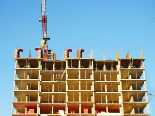 Concrete building under construction. Construction site. Crane near building against the blue sky.
