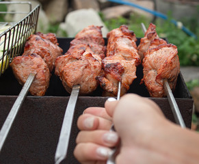 A person roasts a barbecue on the coals. The hand turns the skewers. Barbecue on weekends in summer.