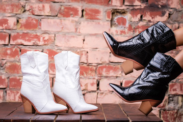 black and White cossack boots leather with a brown heel dressed on a model, on a stone background. Village half. fashion shoes. studio shooting. harmonious legs