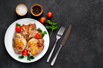 Grilled chicken thighs on a white plate with spices on a stone background with copy space for your text