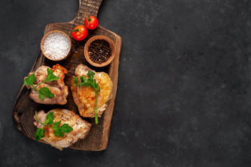 Grilled chicken thighs on a cutting board with spices on a stone background with copy space for your text