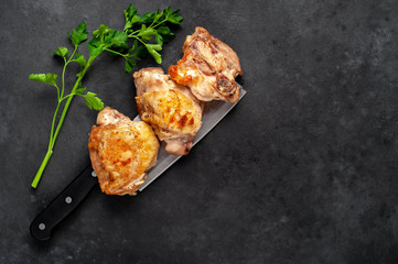 Grilled chicken thighs on a knife with spices on a stone background with copy space for your text