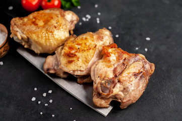 Grilled chicken thighs on a knife with spices on a stone background