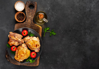 Grilled chicken thighs on a black plate on a cutting board with spices on a stone background with copy space for your text