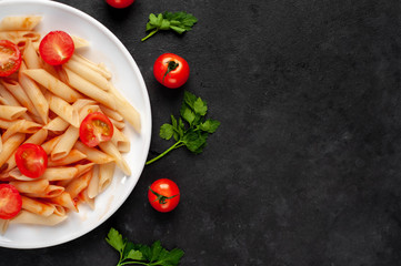
Penne pasta in tomato sauce with tomatoes in a white plate on a stone background with copy space for your text