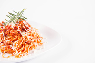 Spaghetti bolognese on a plate decorated with a rosemary twig and sprinkled with cheese