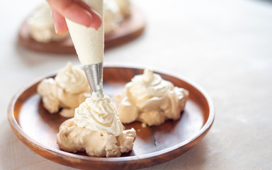 the process of creating Pavlova dessert, decorating the meringue with cream from the culinary bag