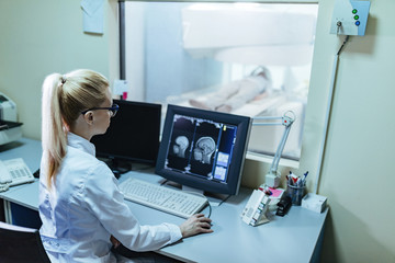Obraz na płótnie Canvas Female radiologist supervising brain scan procedure of a patient from control room.