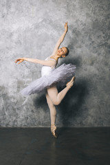 Naklejka na ściany i meble Pretty young ballerina dancer dancing classical ballet against rustic wall