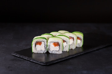 Sushi rolls with salmon, rice, nori, cremette cheese and cucumber slices on a black background.