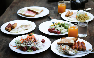 Breakfast set is on the table with sausage, vegetable salad, omelette, ham, bread, fruit, milk, juice, coffee and more. Selective focus. Defocused and blurred image for background.