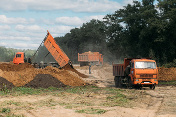 three orange dump trucks at a construction site with sand © dobrovizcki