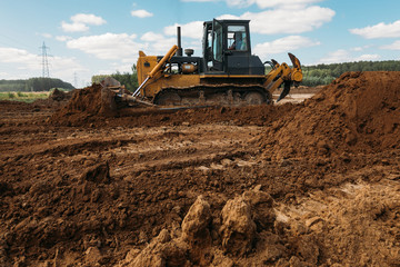 Obraz premium a large yellow old bulldozer at a construction site prepares a site for the construction of a building