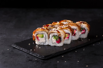 Eel sushi rolls on a stone plate over black background
