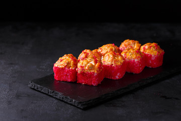 Sushi rolls with grilled salmon, rice, nori, creamy cheese, cucumber and masago on a black background.