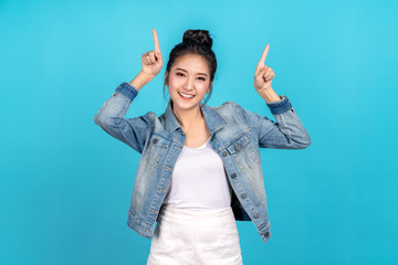 Happy asian woman feeling happiness and standing pointing hands up on blue background.Cute asia girl smiling wearing casual jeans shirt and finger pointing to above for present promotions
