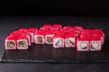 Traditional fresh japanese sushi set rolls on a black stone California ebi . Rolls ingredients: salmon, eel, shrimp, crab, cucumber, red tobik caviar, nori, rice.