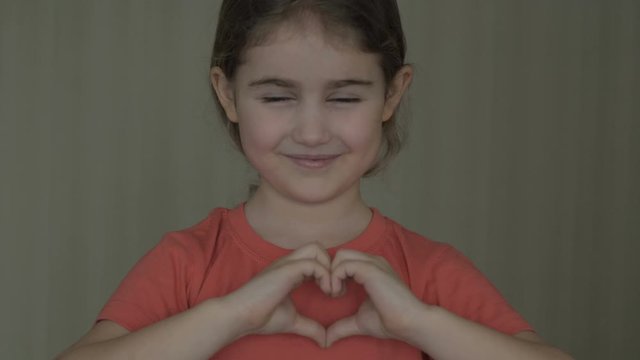 Cute little girl making a heart with her hands and smiling. Young beautiful girl smiling in love showing heart symbol and shape with hands. Romantic concept. Mothers Day.